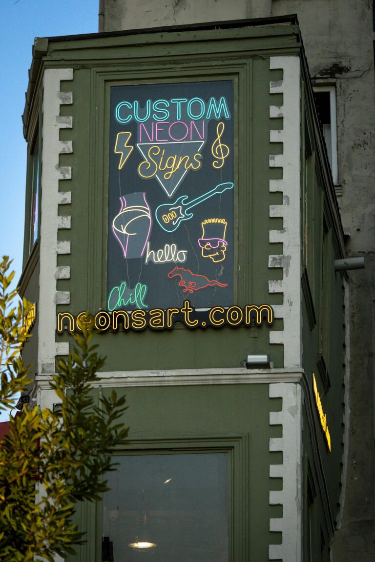 Vibrant neon signs on a building façade displaying custom designs and website information.